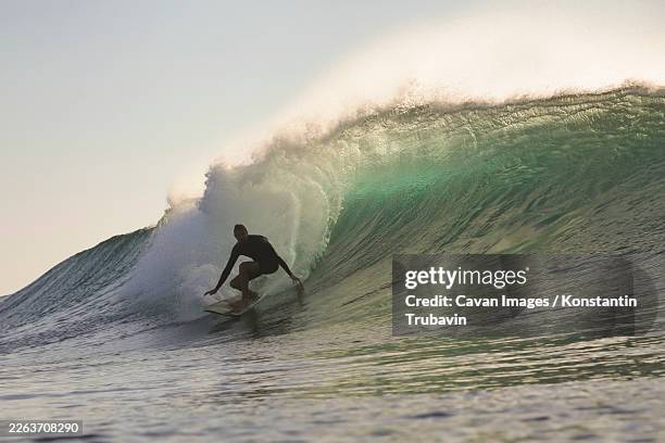 surfer tucked inside translucent barrel at sunset - wave barrel stock pictures, royalty-free photos & images