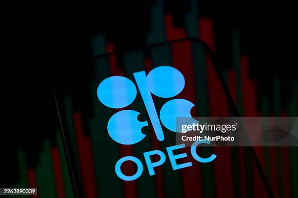 The OPEC logo appears on a smartphone screen placed on a reflective surface onto which a Brent crude oil price chart is projected. The global price...