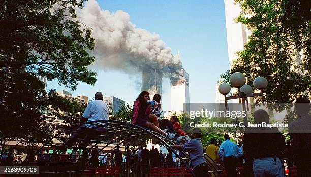 View, over people sitting on a jungle gym in the Charles Venn Park playground , of smoke and flames from the World Trade Center Towers in the wake of...
