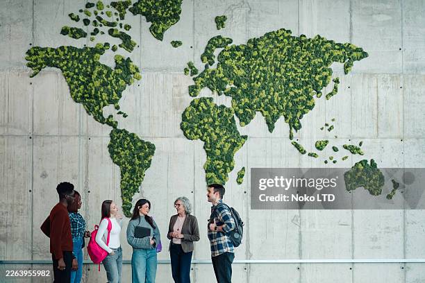 diverse students and mature adult discussion under a green moss world map representing global education and sustainability - global village stock pictures, royalty-free photos & images