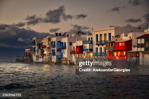 Pequena Veneza Mykonos ao Entardecer: Casas coloridas à beira-mar com varandas com vista para o Mar Egeu Pequena Veneza Mykonos ao Entardecer: Casas coloridas à beira-mar com varandas com vista para o Mar Egeu