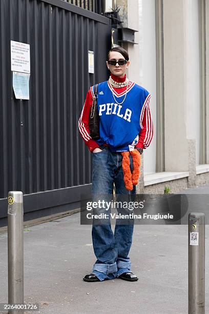 Guest wears black sunglasses, a red turtle neck Adidas jacket, a blue printed gilet, gold and pearl necklaces, an orange fur charm, blue low waist...