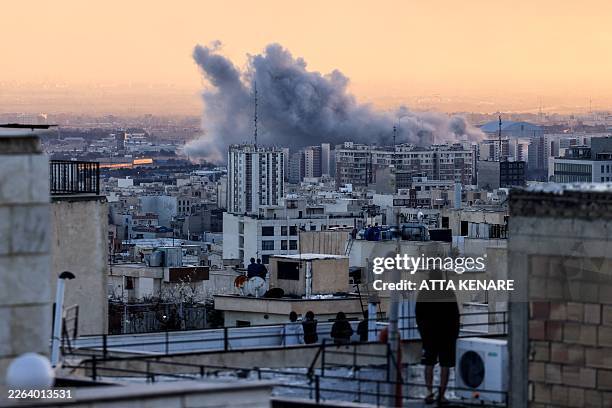 Person stands on the roof of a building looking at a plume of smoke rises after a strike on the Iranian capital Tehran, on March 3, 2026. Iran...