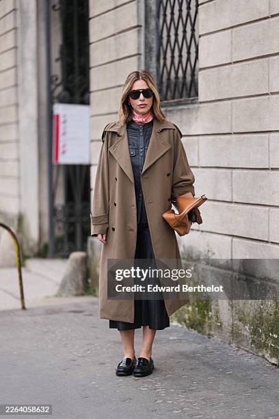 Guest wears black sunglasses, a brown cotton trench coat, a black leather button-front shirt, a pink silk small scarf, black leather wide-leg cropped...