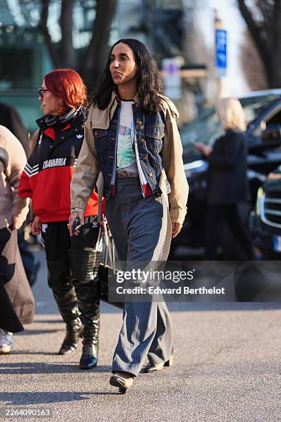 Guest wears a beige cotton jacket with a blue denim panel, a white cotton graphic T-shirt, gray pinstriped wide leg trousers, a black leather bag,...
