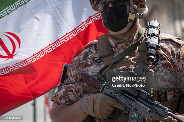 An armed military member of the Islamic Revolutionary Guard Corps holds an AK-45 rifle and stands guard outside a police facility that is destroyed...