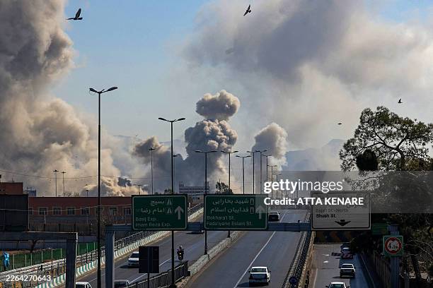 Motorists drive along an expressway as plumes of smoke rise after a strike in Tehran on March 5, 2026. Israel pounded Tehran with fresh strikes and...