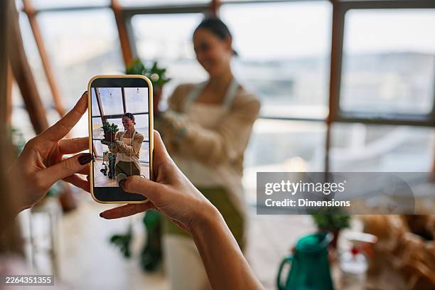 woman photographing colleague with potted plant for small business social media content in studio - behind the scenes stock pictures, royalty-free photos & images