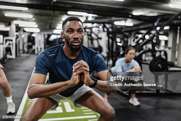 focused man performing squat workout in modern gym with other athletes training - bodyweight training stock pictures, royalty-free photos & images