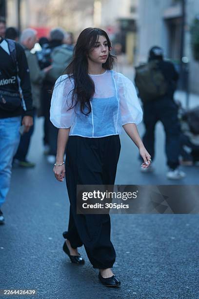 Person is seen wearing silver hoop earrings, a white sheer puff-sleeve top, a blue corset-style top, black voluminous harem-style trousers, black...