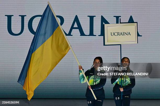 Volunteers hold a flag of Ukraine and a placard during the delegation part of the Milano Cortina 2026 Winter Paralympic Games opening ceremony at...
