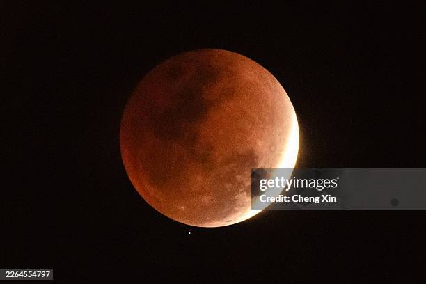 Total lunar eclipse transitions into the partial phase as sunlight begins to reappear on the lunar surface while a star appears just below the moon's...