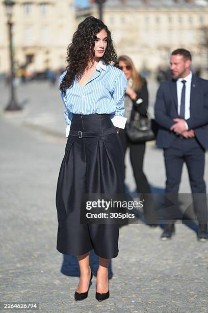 Deva Cassel is seen wearing brown tortoiseshell sunglasses, a Dior blue and white striped button-down shirt with white cuffs, a black high-waisted...