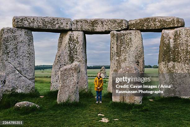 girl in yellow coat smiles with stonehenge stones in green grass - stonehenge stock pictures, royalty-free photos & images