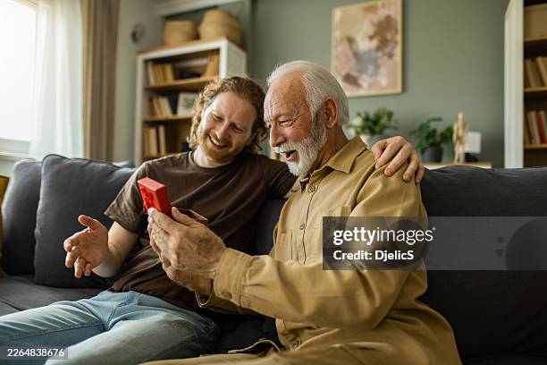 grandfather opening gift from adult son feeling surprised - fathers day stock pictures, royalty-free photos & images