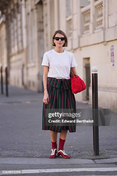 Monica Ainley de La Villardiere wears light brown bob haircut, black sunglasses, a white cotton crew neck t-shirt, a dark green striped print pattern...