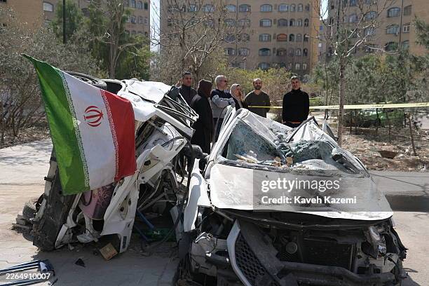 The neighbors standing by a destroyed car with an Islamic Republic flag look at the building damaged in Shahid Borujerdi residential complex in south...