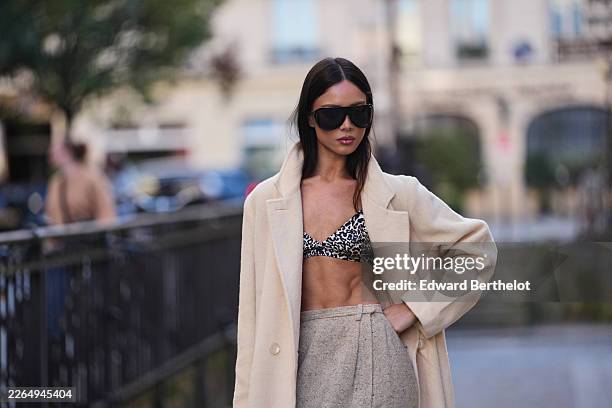 Guest wears straight black hair, black futurist sunglasses, a cream wool long coat, a black and white animal print bra top, a gray wool high waist /...