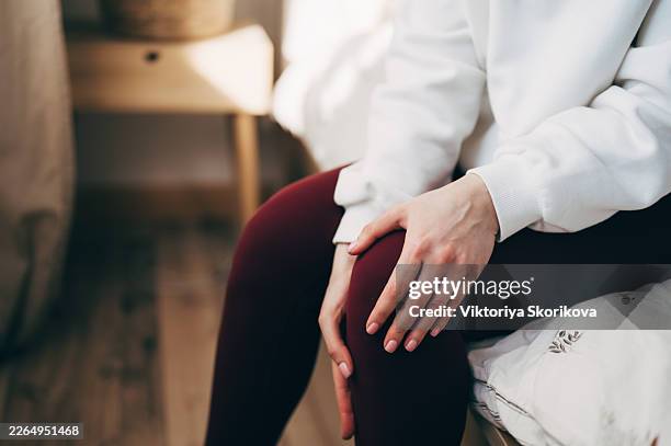 female is sitting on mat and touching joint while suffering pain during video workout on laptop at home - rheumatism stock pictures, royalty-free photos & images