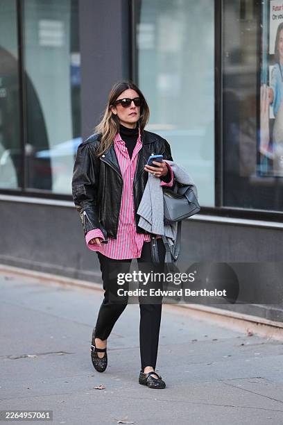 Guest wears dark brown hair, black sunglasses, a black leather biker jacket, a pink and white cotton striped button-down shirt, a black knit...