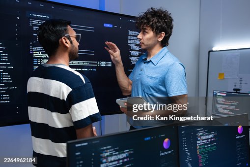 Two Software Developer, Computer Programmer working together in control room. Male Leader Software Engineer Explaining Code on Screen to Colleagues, Discussion and Brainstorm Collaboration work in office. Two Software Developer, Computer Programmer working together in control room. Male Leader Software Engineer Explaining Code on Screen to Colleagues, Discussion and Brainstorm Collaboration work in office.