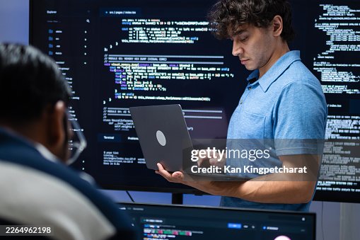 Programmer Working with Laptop and Code Display, Reviewing Software Tasks While Standing in Front of a Large Programming Screen in Modern Tech Office. Programmer Working with Laptop and Code Display, Reviewing Software Tasks While Standing in Front of a Large Programming Screen in Modern Tech Office.