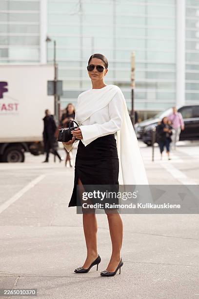Gili Biegun wears a white draped asymmetric blouse with wide flared sleeve paired with a black high-waisted pencil skirt with front slit, aviator...