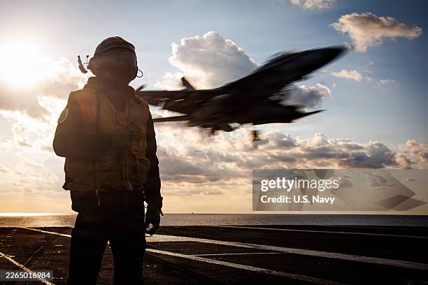 In this handout photo provided by the U.S. Navy, A U.S. Sailor serves as arresting gear officer as an F/A-18F Super Hornet aircraft, attached to...