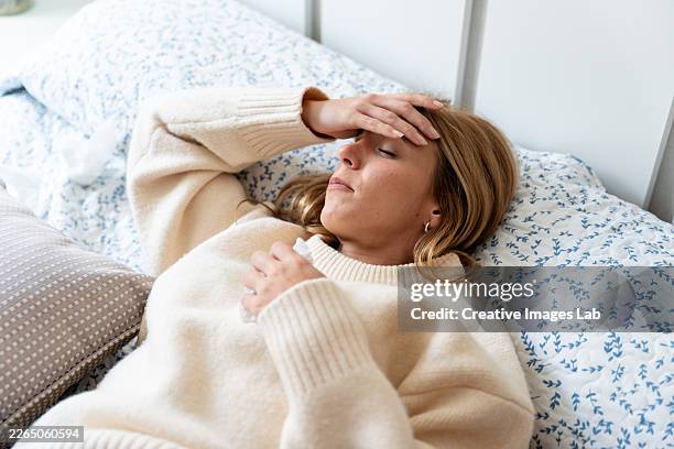 young adult woman feeling ill with headache resting in bed - uncomfortable stock pictures, royalty-free photos & images
