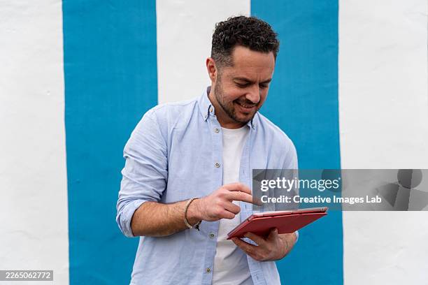 smiling man using digital tablet outdoors against striped wall - camisa azul fotografías e imágenes de stock