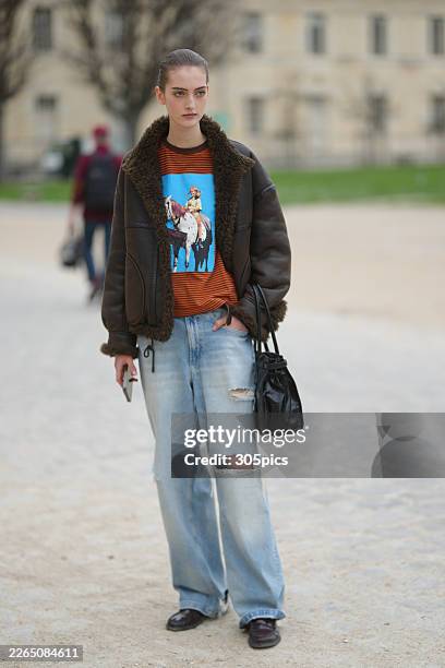 Person is seen wearing a brown shearling-lined leather aviator jacket, an orange and black striped graphic t-shirt featuring a horse and rider motif,...