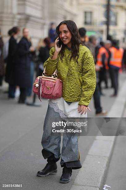 Guest is seen wearing an olive green quilted floral-patterned jacket, a white lace-trimmed asymmetrical slip top over blue denim wide-leg trousers...