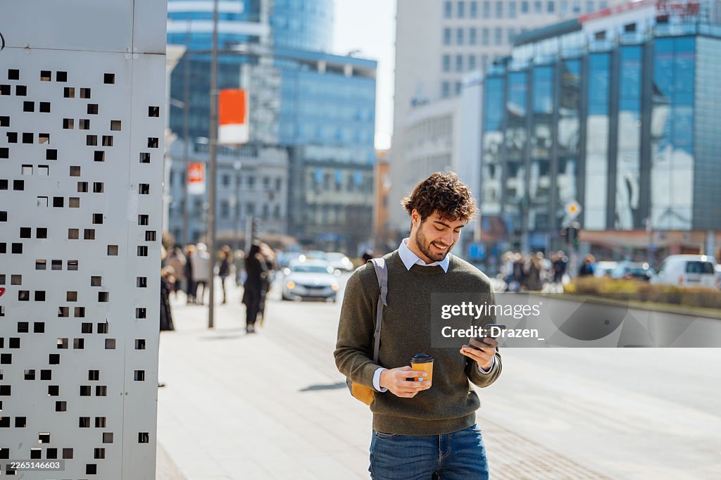 Joven usando el smartphone mientras sostiene café al aire libre