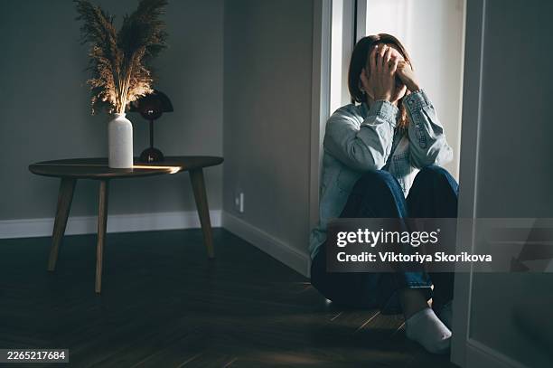 depressed woman sitting on floor covering face with hands in despair - mishandeling stockfoto's en -beelden