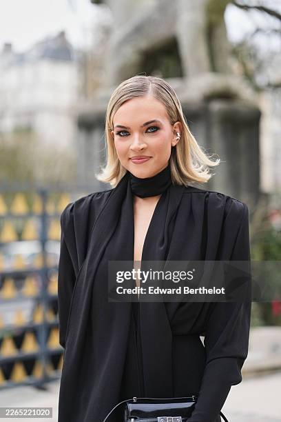 Emilia Silberg wears a black woven long sleeve / shoulder pads / wrap tulle fitted midi dress with a black woven scarf detail, a black varnished...