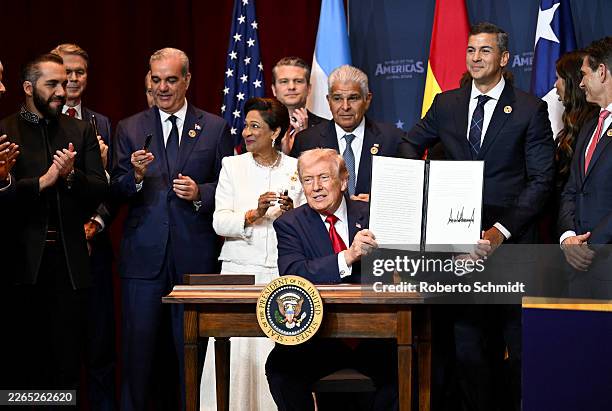 President Donald Trump holds a document that indicates a U.S. "Commitment to Countering Cartel Criminal Activity" that he signed while surrounded by...