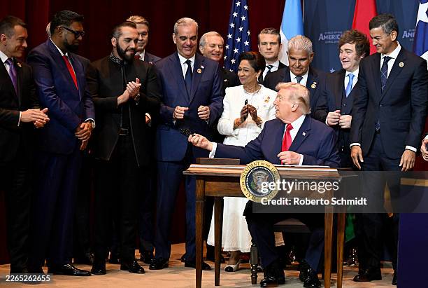 President Donald Trump holds hands out pens after signing a document that indicates a U.S. "Commitment to Countering Cartel Criminal Activity" while...
