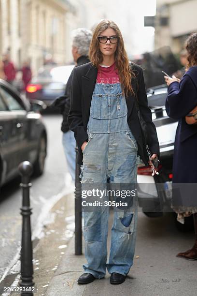 Betsy Gaghan is seen wearing black tortoiseshell glasses, a black wool pea coat, a red graphic t-shirt, light blue distressed and patched denim...