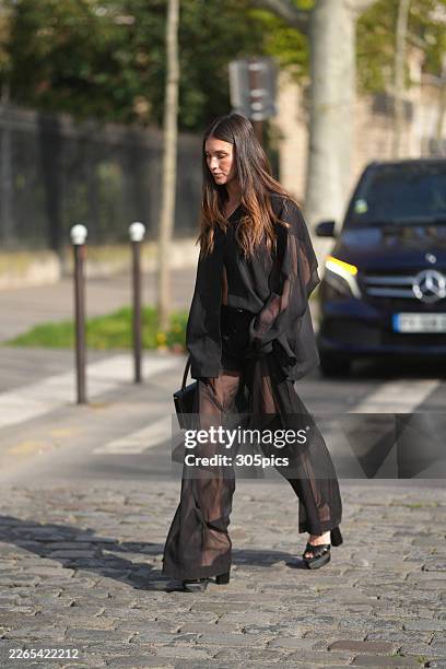 Rainey Qualley is seen wearing an Akris black button-down sheer shirt, black wide-leg sheer trousers, black platform heels, while carrying a black...
