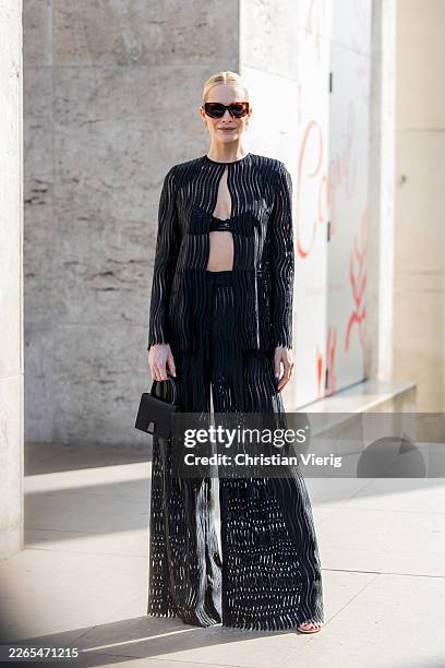 Poppy Delevingne wears black cropped top, transparent long sleeved blouse, flared wide leg ripped pants, bag, sunglasses outside Akris during Day...