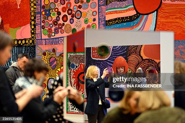 Visitors take photos beside a photo of Japanese artist Yayoi Kusama next to of her artwork "My Eternal Soul series" during a preview for an...