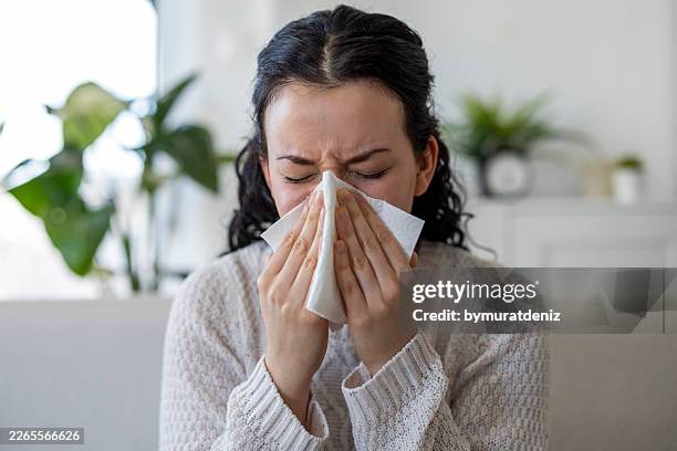 sick young woman blowing her nose with tissue on sofa - sinusitis stock pictures, royalty-free photos & images