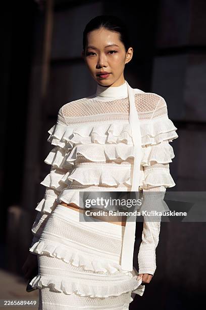 Guest wears a white long-sleeve ruffled cropped top with sheer panels and a matching high-waisted ruffled maxi skirt, a white crossbody strap outside...