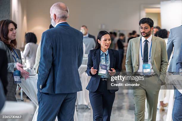 asian businesswoman and indian businessman engaging in conversation at conference event - business conference stock pictures, royalty-free photos & images