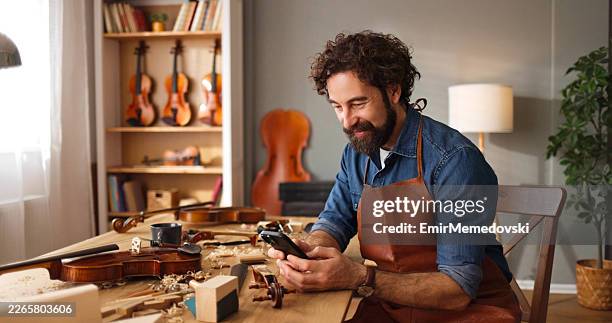 kunsthandwerker geigenbauer mit smartphone in der werkstatt - kunsthandwerker stock-fotos und bilder
