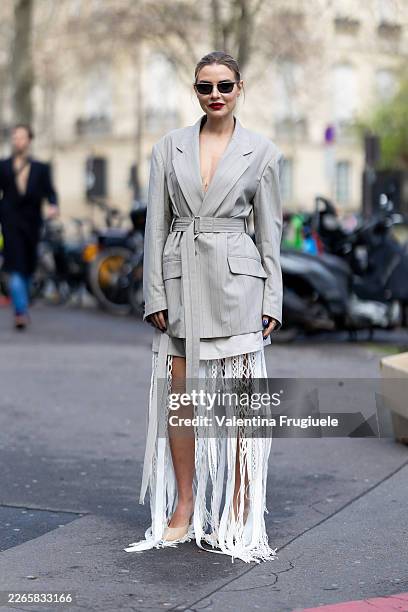 Veronica Ferraro wears black sunglasses, a grey jacket, beige suede pumps and a white long dress with lace fringes outside Ujho show during Day Nine...