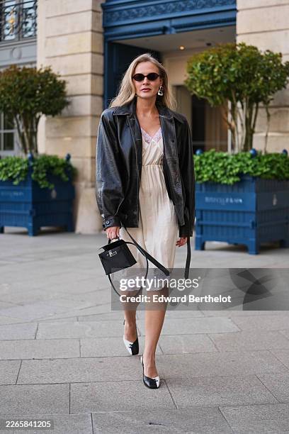 Guest wears sunglasses, a black leather jacket, a white lace V-neck / belted knees dress, a black leather handbag, black and white bicolored leather...