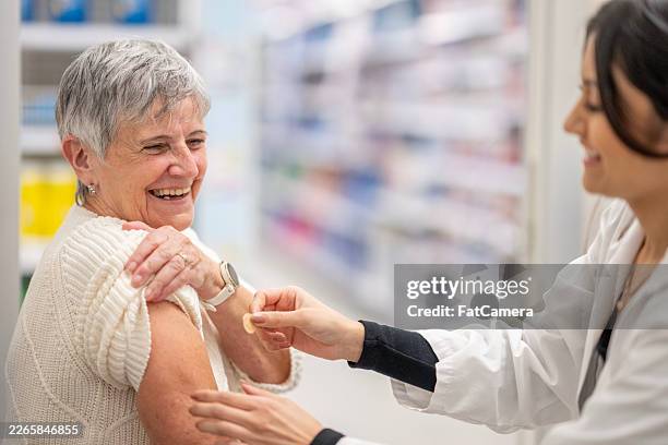 elderly caucasian woman receiving arm vaccination from asian healthcare professional in pharmacy - flu shot stock pictures, royalty-free photos & images