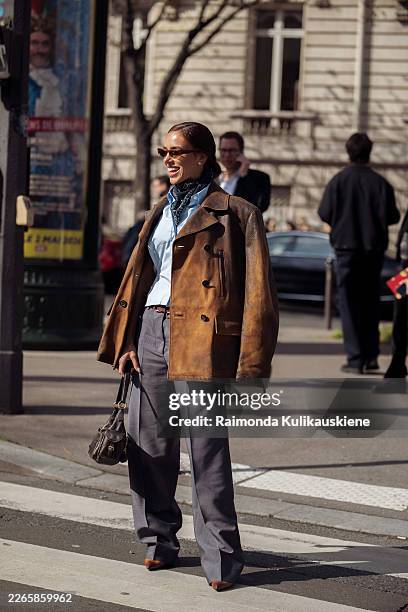 Bruna Biancardi wears a brown leather jacket layered over a light blue button-up shirt and patterned neck scarf paired with grey wide-leg trousers,...