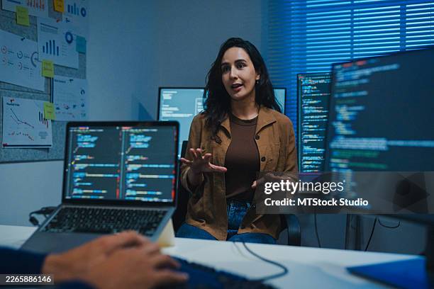 young latin software developers team meeting discussing source code on desktop monitor working late in the dark office at night. artificial intelligence and programming. - java code stock pictures, royalty-free photos & images